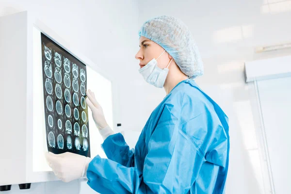 Vista lateral del atractivo médico en gorra médica y radiografía de retención uniforme en la clínica - foto de stock