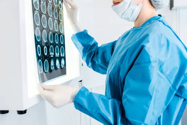 Cropped view of doctor in medical cap and uniform holding x-ray in clinic — Stock Photo