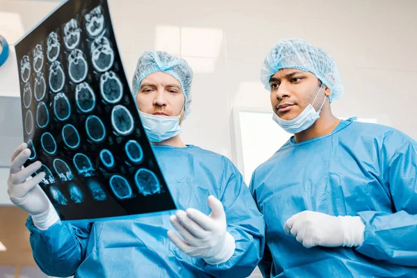 Médicos guapos en uniformes y máscaras médicas hablando de rayos X en la clínica - foto de stock