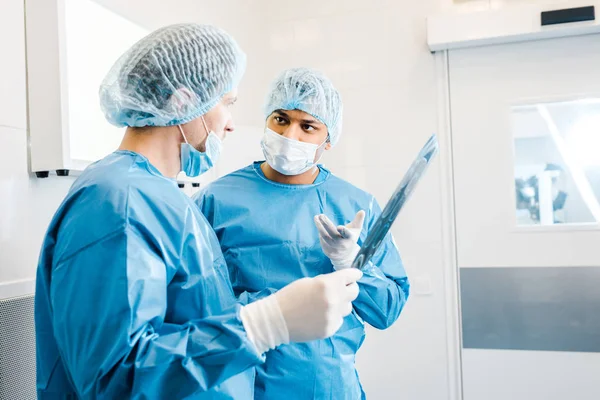 Лікарі в уніформі та медичні маски говорять про рентген в клініці — стокове фото