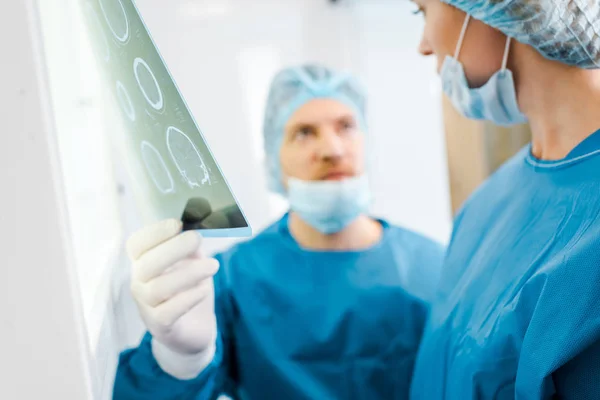 Foco seletivo de médicos em uniformes e máscaras médicas falando sobre raio-x na clínica — Stock Photo