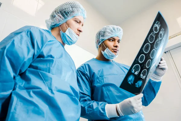 Низкий угол обзора красивых врачей в униформе и медицинских масках, смотрящих на рентген — стоковое фото