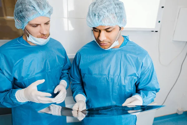 Médicos guapos en uniformes y máscaras médicas hablando de rayos X - foto de stock