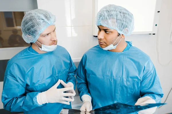 Симпатичные врачи в форме и медицинских масках говорят о рентгене — стоковое фото