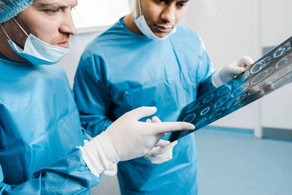 Selektive Fokussierung von Ärzten in Uniformen und medizinischen Masken, die mit dem Finger auf Röntgenaufnahmen zeigen — Stockfoto