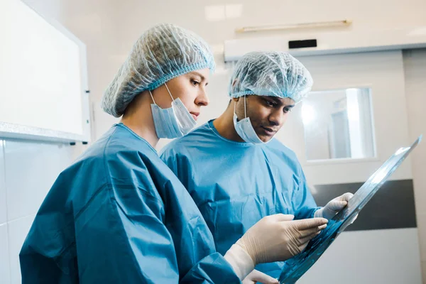 Médicos bonitos e bonitos em uniformes e máscaras médicas olhando para raio-x — Fotografia de Stock