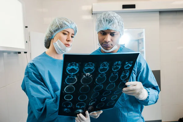Good-looking and beautiful doctors in uniforms and medical masks talking about x-ray — Stock Photo