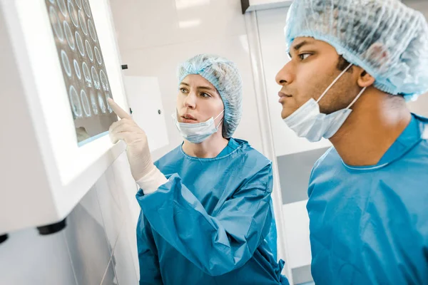 Médicos bonitos e bonitos em uniformes e máscaras médicas apontando com o dedo para o raio-x — Fotografia de Stock