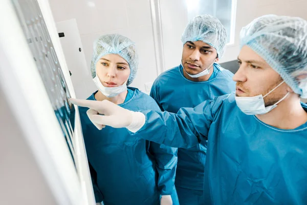 Красивых и красивых врачей в униформе и медицинских масках, указывающих пальцем на рентген — стоковое фото