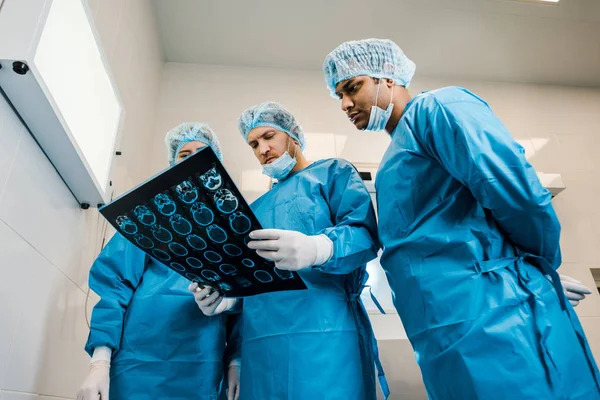 Vista de ángulo bajo de los médicos guapos y hermosos en uniformes y máscaras médicas hablando de rayos X - foto de stock