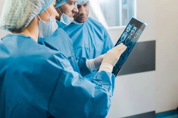 Handsome and attractive doctors in uniforms and medical masks talking about x-ray — Stock Photo