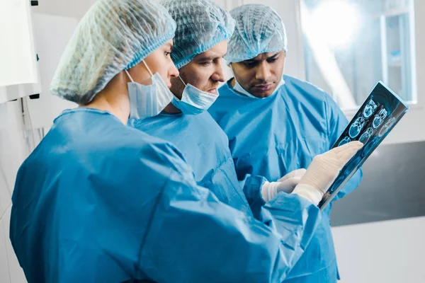 Handsome and attractive doctors in uniforms and medical masks talking about x-ray — Stock Photo