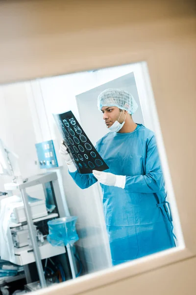 Красивий лікар в уніформі та медичній кепці, дивлячись на рентген в клініці — стокове фото