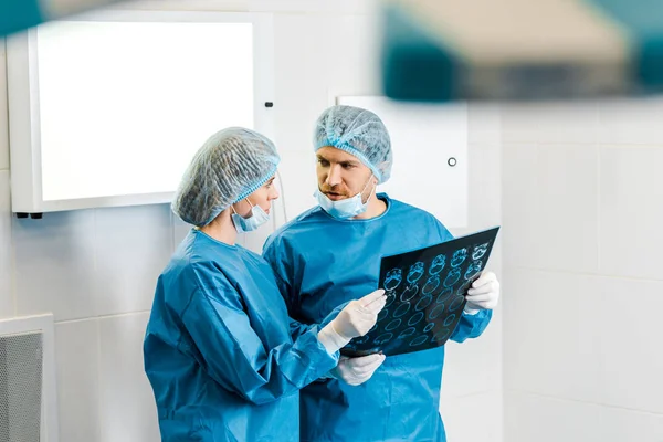 Enfoque selectivo de guapos y hermosos médicos en uniformes que sostienen rayos X y hablar - foto de stock