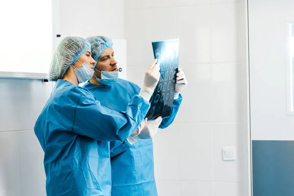 Guapos y hermosos doctores en uniformes sosteniendo rayos X y hablando - foto de stock