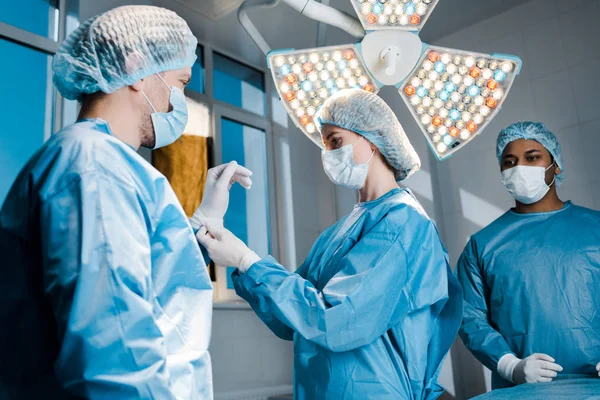 Infermiera in uniforme e maschera medica mettere guanto di lattice a portata di mano del medico — Foto stock