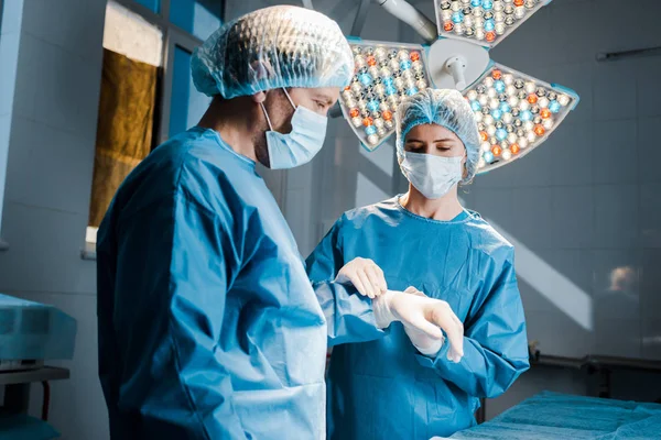 Enfermeira de uniforme e máscara médica colocando luva de látex na mão do médico — Stock Photo