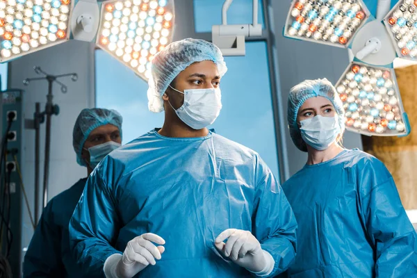 Médicos y enfermeras en uniformes y máscaras médicas mirando hacia otro lado en el quirófano - foto de stock