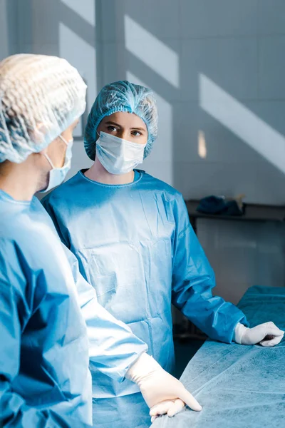 Selective focus of nurse and doctor in uniforms and medical masks looking at each other — Stock Photo