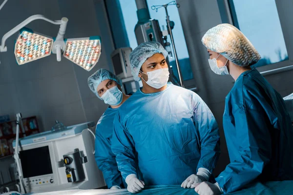 Médicos y enfermeras en uniformes y máscaras médicas hablando en quirófano - foto de stock