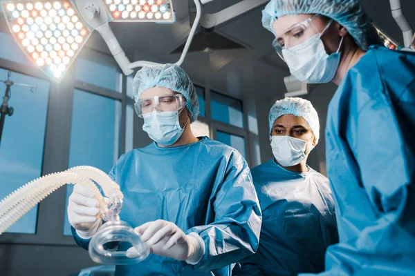 Doctors and nurse in uniforms and medical caps holding mask in operating room — Stock Photo