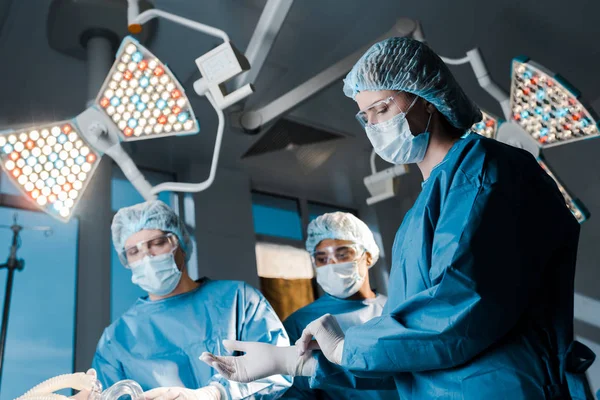 Вибірковий фокус лікарів і медсестер в уніформі і медичних шапочках в операційній кімнаті — стокове фото