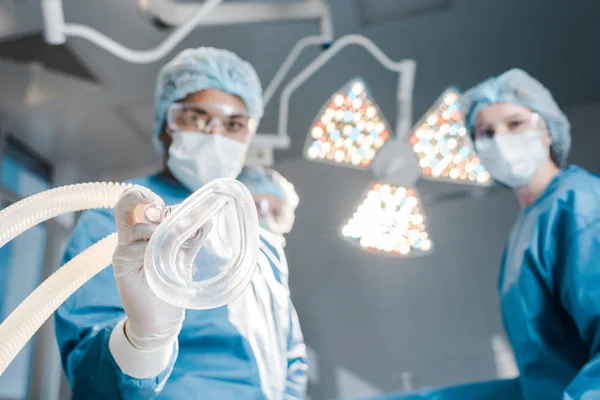 Selective focus of doctor and nurse in uniforms and medical caps holding mask — Stock Photo