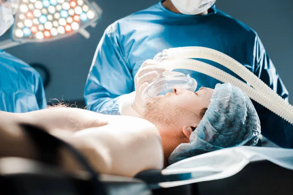 Cropped view of doctor in uniform putting mask on patient in operating room — Stock Photo