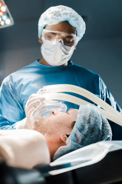 Foco seletivo do médico em uniforme e tampa médica colocando máscara no paciente — Fotografia de Stock