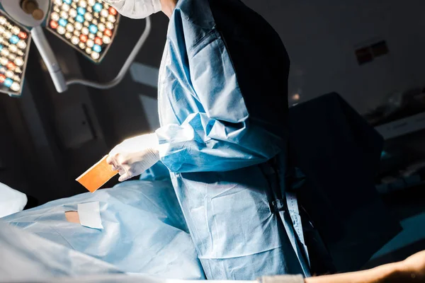 Vista recortada de la enfermera en uniforme y guantes de látex que se ponen en tira en el quirófano - foto de stock