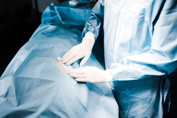 Visão parcial do enfermeiro de uniforme e luvas de látex colocando tira na sala de cirurgia — Fotografia de Stock