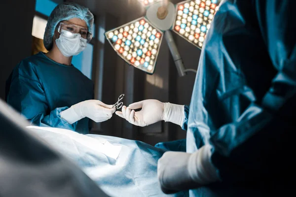 Selektiver Fokus der Krankenschwester in Uniform und medizinischer Maske, die dem Chirurgen medizinisches Gerät gibt — Stockfoto