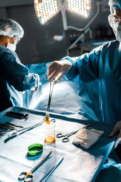 Selective focus of surgeon doing operation and nurse holding tampon in operating room — Stock Photo