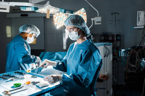 Cirurgião fazendo operação e enfermeira segurando tampão na sala de cirurgia — Fotografia de Stock