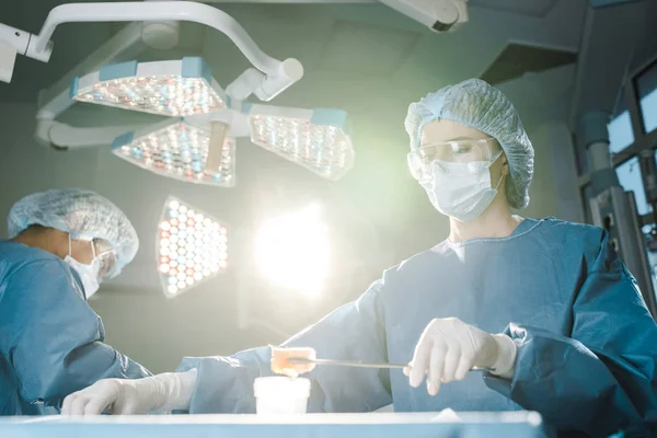 Chirurgien faisant une opération et infirmière en uniforme tenant tampon dans la salle d'opération — Photo de stock
