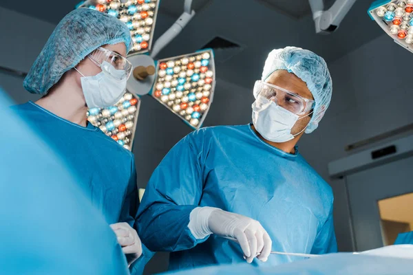 Enfermeira de uniforme e cirurgião de boné médico olhando um para o outro na sala de cirurgia — Fotografia de Stock