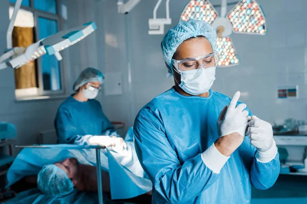 Selective focus of doctor in uniform putting off latex gloves in operating room — Stock Photo