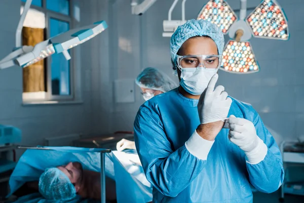 Messa a fuoco selettiva del medico in uniforme rimandando i guanti in lattice in sala operatoria — Foto stock