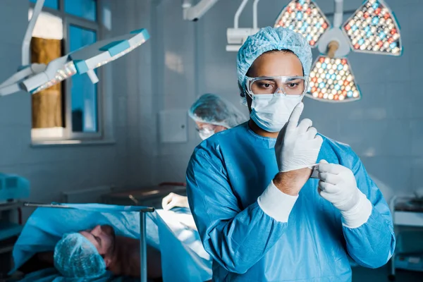 Selective focus of doctor in uniform putting off latex gloves in operating room — Stock Photo