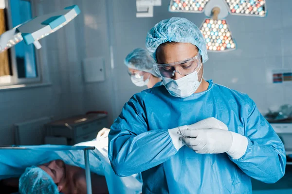 Messa a fuoco selettiva del medico in uniforme rimandando i guanti in lattice in sala operatoria — Foto stock