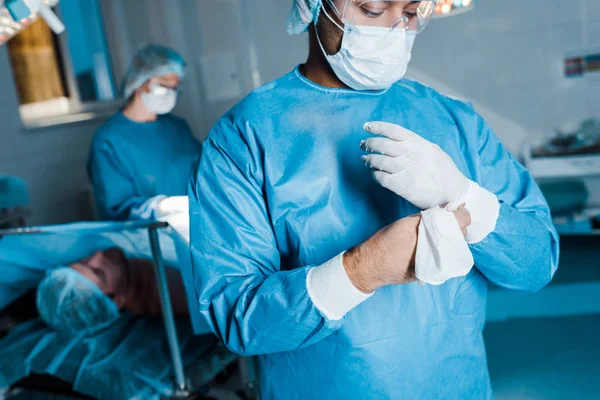 Selective focus of doctor in uniform putting off latex gloves in operating room — Stock Photo