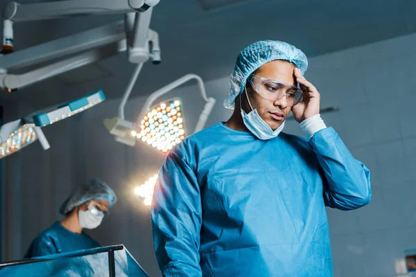 Foyer sélectif du médecin en uniforme et masque médical regardant vers le bas dans la salle d'opération — Photo de stock