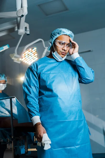 Focalizzazione selettiva del medico in uniforme e maschera medica distogliendo lo sguardo in sala operatoria — Foto stock
