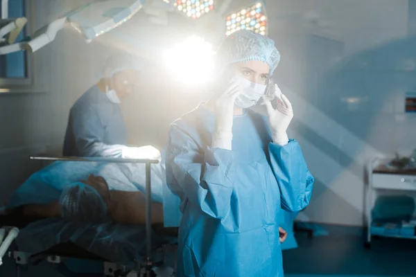 Selektiver Fokus der Krankenschwester in Uniform und medizinischer Maske, die die Brille im Operationssaal ablegt — Stockfoto