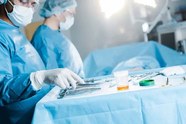 Foco seletivo de cirurgião e enfermeiro em uniforme e máscara médica segurando equipamentos médicos — Fotografia de Stock