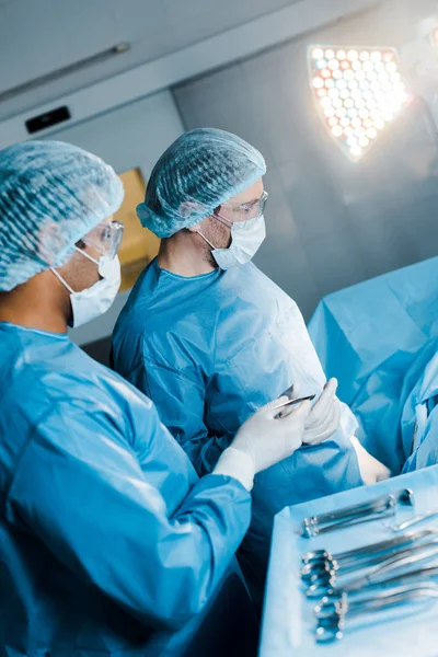 Enfermeira de uniforme e máscara médica dando equipamentos médicos ao cirurgião — Fotografia de Stock