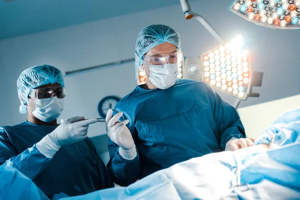 Enfermera en uniforme y máscara médica que da equipo médico al cirujano - foto de stock