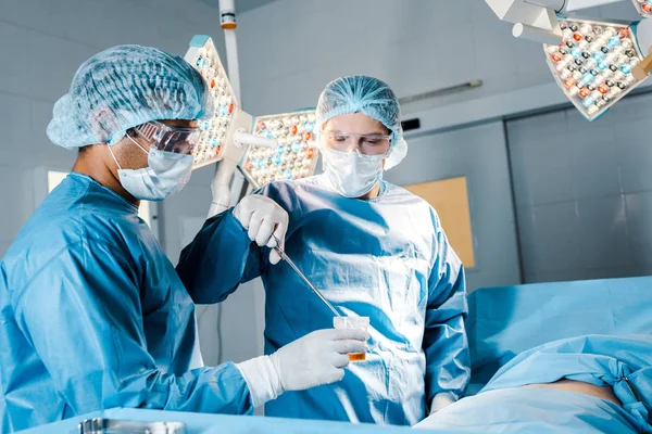 Медсестра и хирург в форме и медицинских масках, выполняющие операции в операционной — стоковое фото