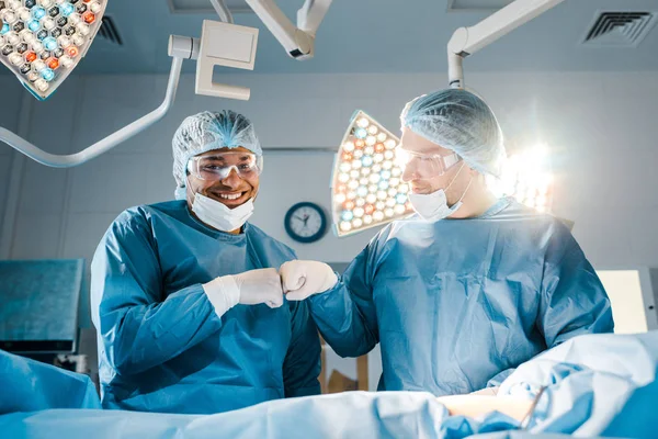 Enfermera y cirujano en uniformes haciendo gesto y sonriendo en quirófano - foto de stock