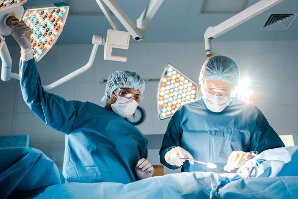 Infirmière et chirurgienne en uniforme et masques médicaux parlant en salle d'opération — Photo de stock